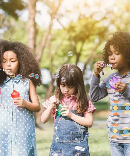 Three young girls blowing bubbles in a park.